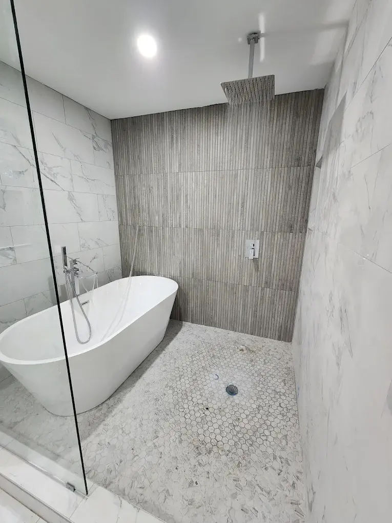 Walk-in shower with rain shower head and freestanding tub on marble tile